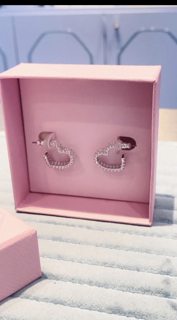 A pair of sparkling heart-shaped earrings displayed in a pink gift box.