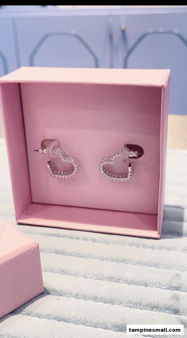 A pair of sparkling heart-shaped earrings displayed in a pink gift box.