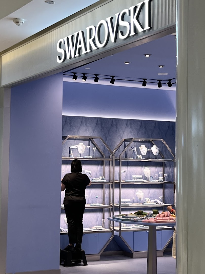 The image shows the entrance of a Swarovski store with a staff member inside arranging displays.