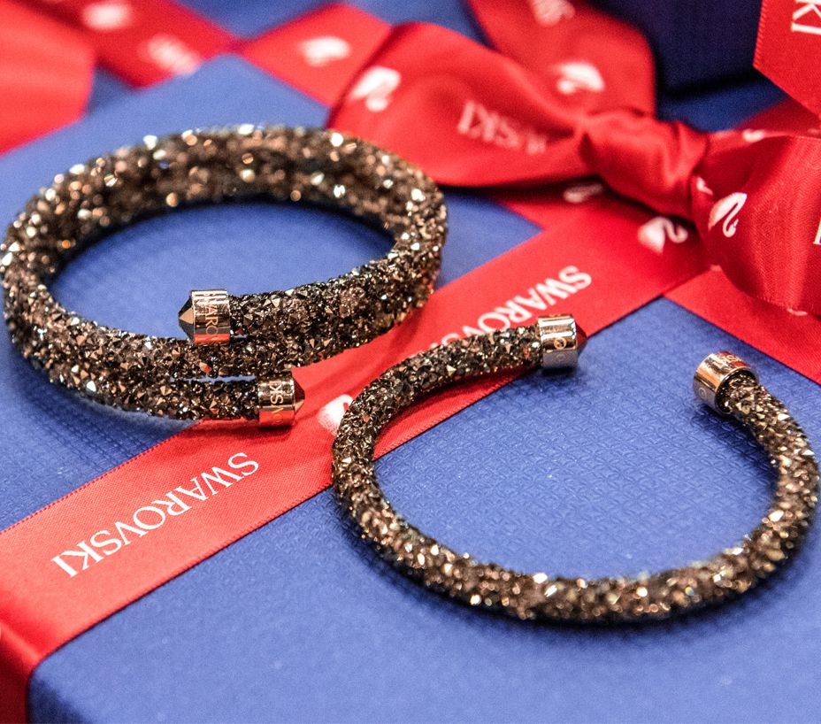 Two sparkling Swarovski crystal bracelets displayed on a blue gift box with a red branded ribbon.