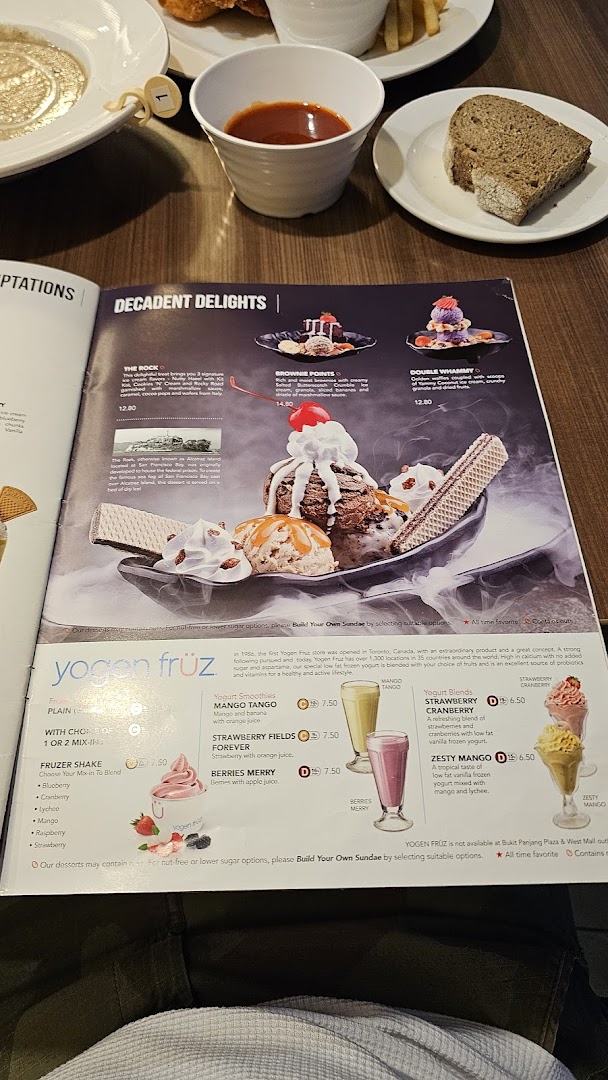 A Swensen's menu displays decadent ice cream sundaes and refreshing yogurt desserts, with food on a table.