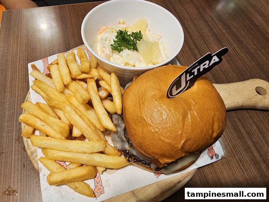 A delicious burger, golden fries, and creamy coleslaw served on a wooden board.