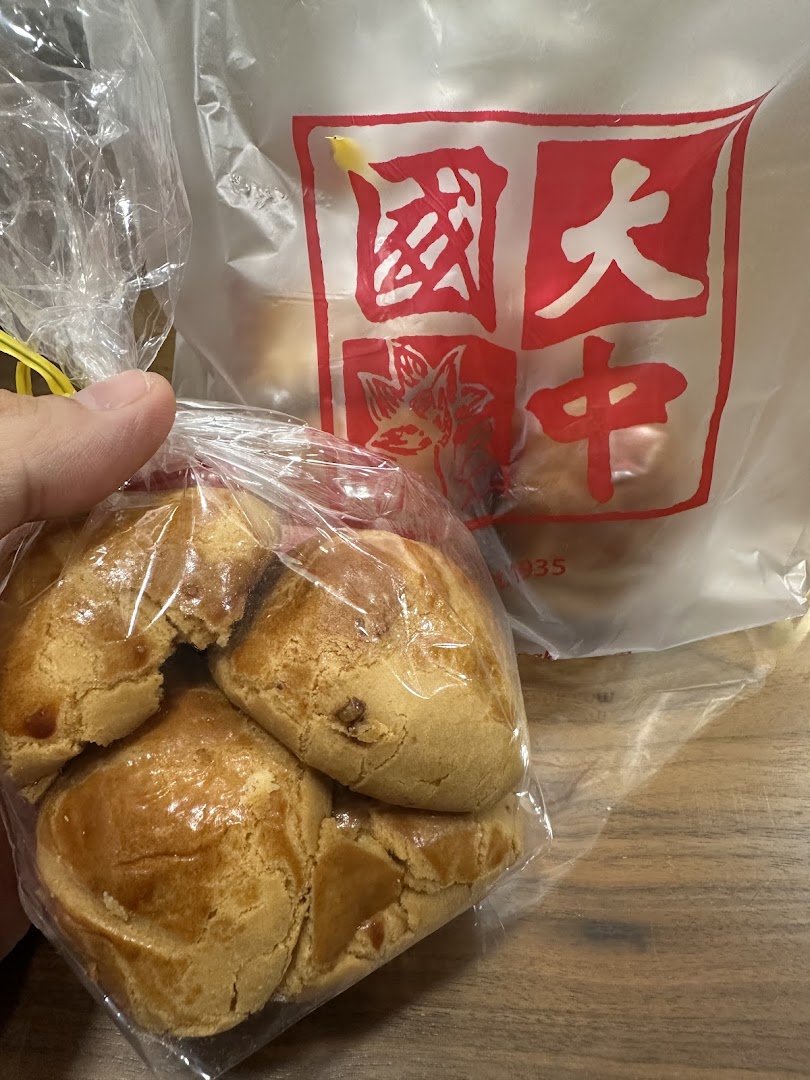 A hand holds a bag of golden-baked pastries, with a Tai Chong Kok branded paper bag visible in the background.