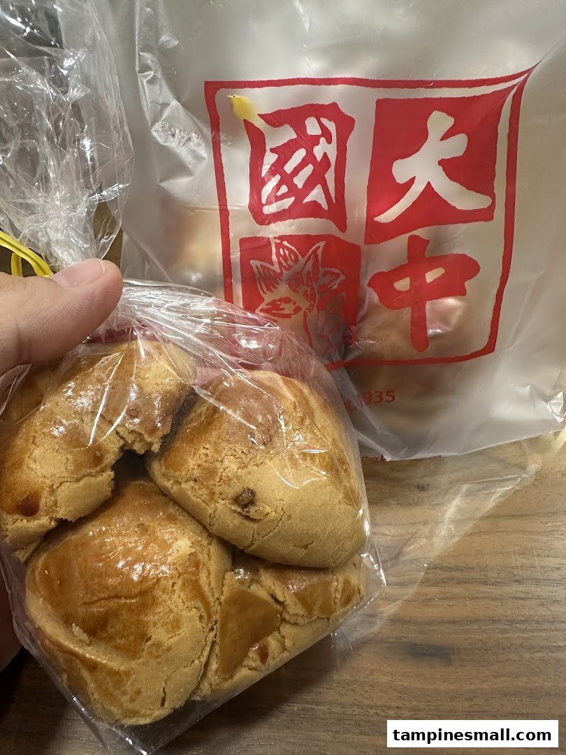 A hand holds a bag of golden-baked pastries, with a Tai Chong Kok branded paper bag visible in the background.