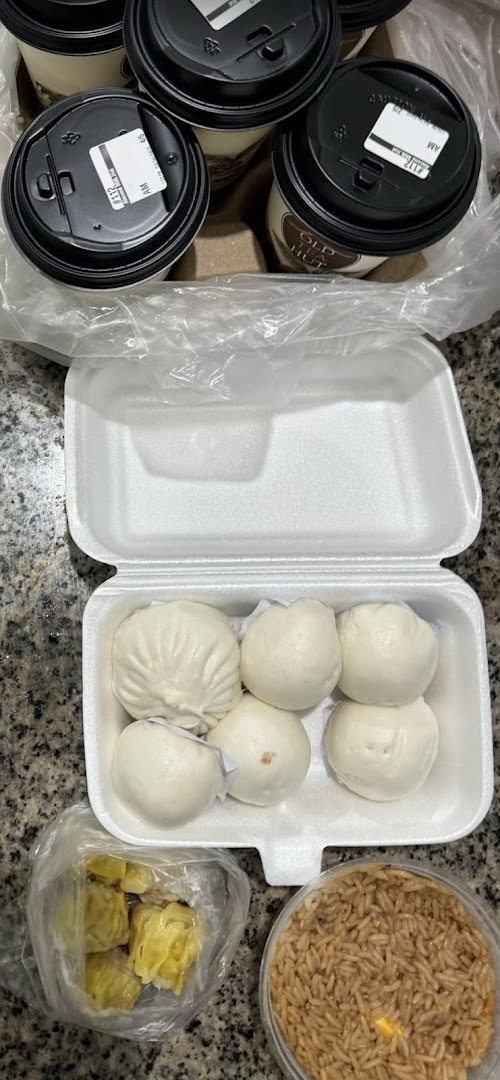 An assortment of freshly steamed buns, siew mai, and rice, accompanied by coffee cups.