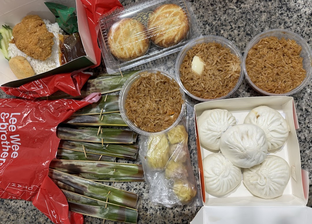 A diverse spread of Asian takeaway food, including steamed buns, fried rice, Nasi Lemak, Otah, and pastries.