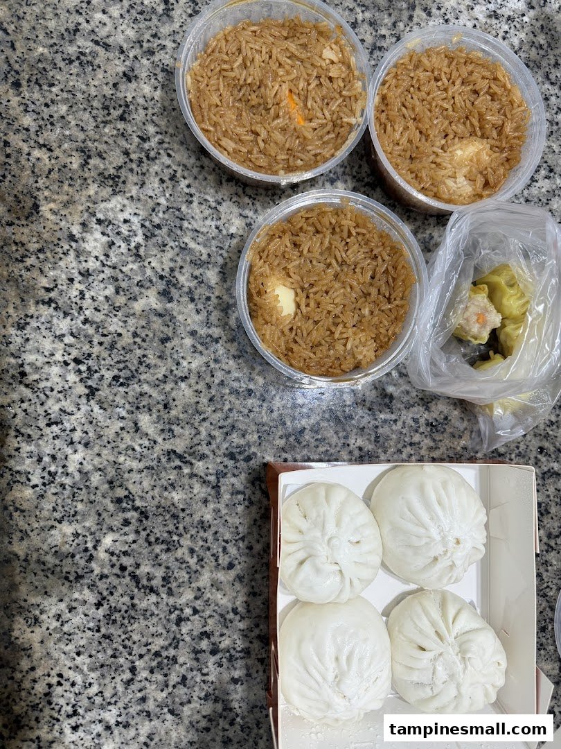 A top-down view of various food items including rice, paus, and dim sum on a granite surface.