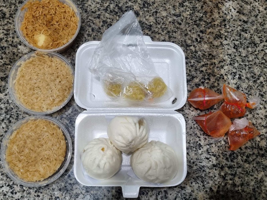 Assorted steamed buns, glutinous rice, and chili sauce in takeout containers on a granite surface.