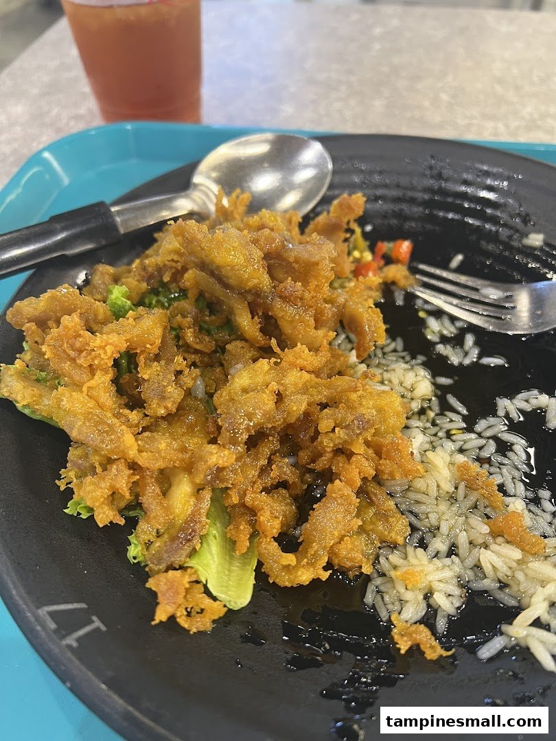 A close-up of a delicious crispy fried dish with rice and greens on a black plate.