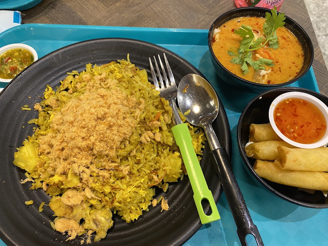 A vibrant meal featuring pineapple fried rice, tom yum soup, and crispy spring rolls on a blue tray.