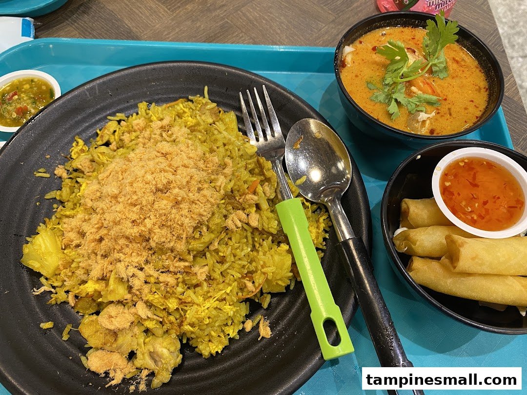 A vibrant meal featuring pineapple fried rice, tom yum soup, and crispy spring rolls on a blue tray.