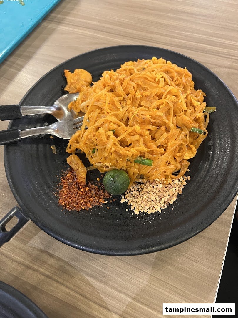 A vibrant plate of Pad Thai noodles with lime, chili flakes, and crushed peanuts.