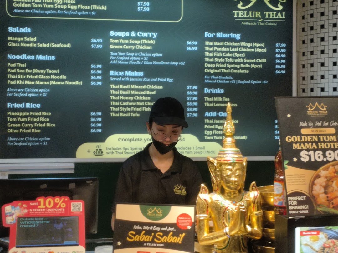 A Telur Thai counter with a prominent menu board, staff member, and a golden statue.