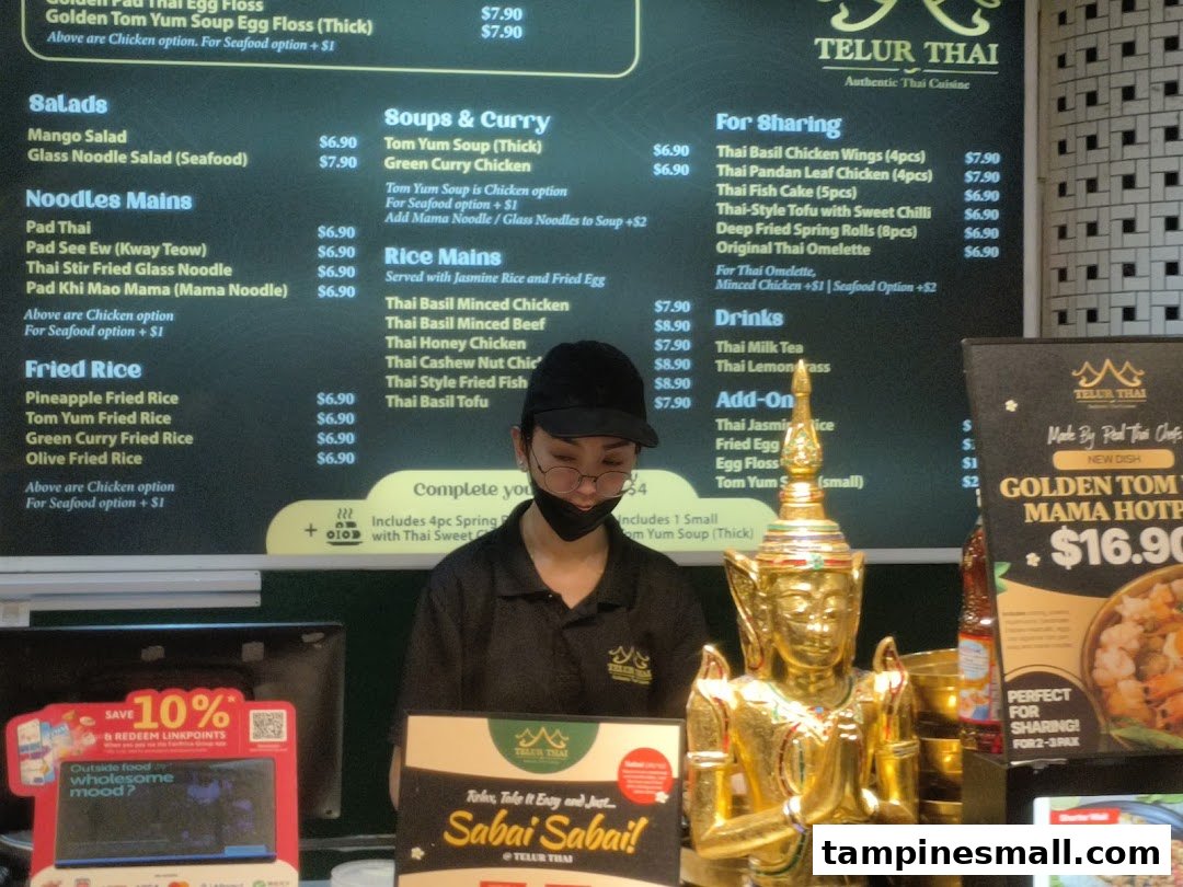A Telur Thai counter with a prominent menu board, staff member, and a golden statue.