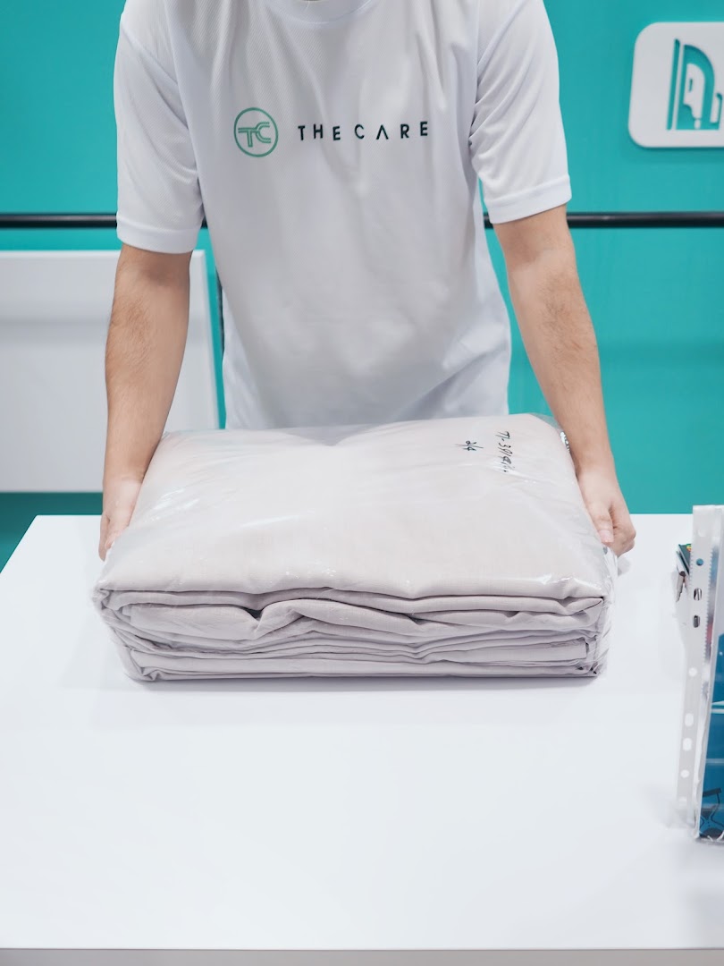 A staff member from The Care Laundry presents a neatly packaged, freshly laundered item on a clean counter.