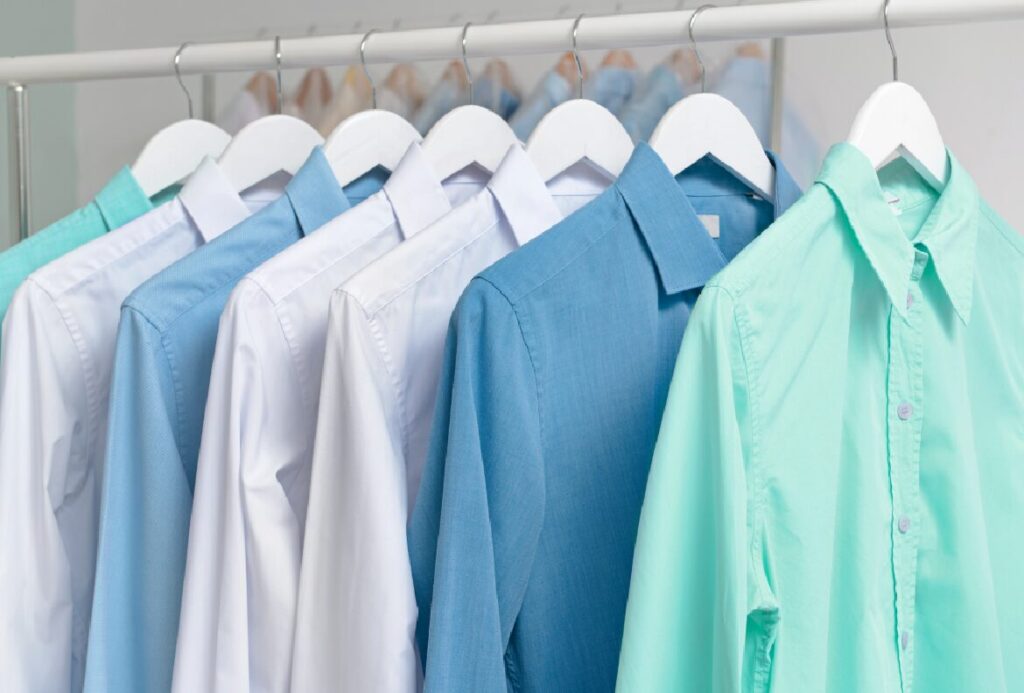 Clean, pressed shirts in various shades of blue and white hanging neatly on a laundry rack.