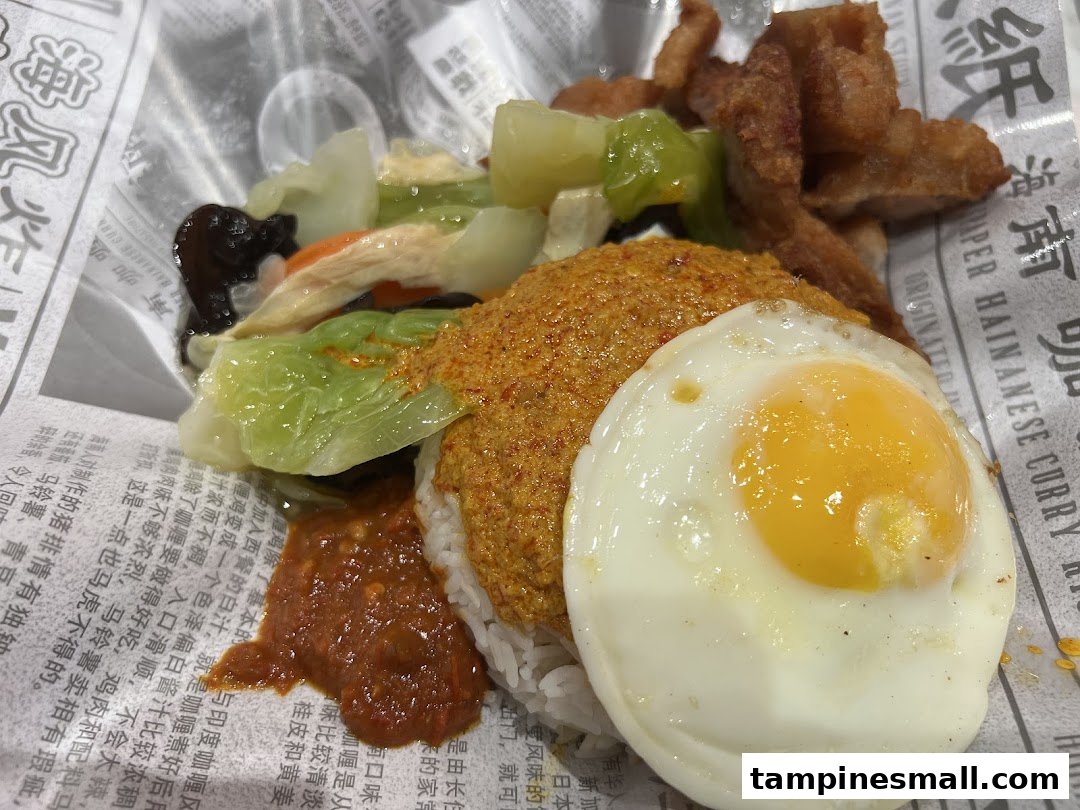 A close-up of Hainanese curry rice with fried chicken, vegetables, and a sunny-side-up egg.