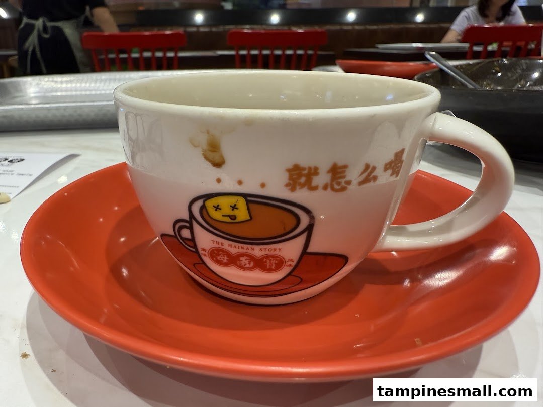 A white coffee cup with a unique cartoon design and Chinese characters, resting on a red saucer.