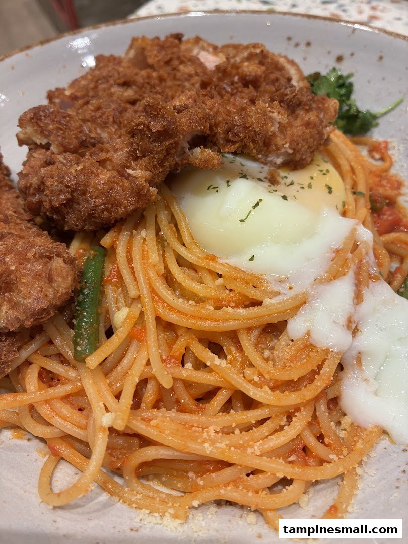 A close-up of spaghetti with crispy fried chicken cutlet and a creamy poached egg.