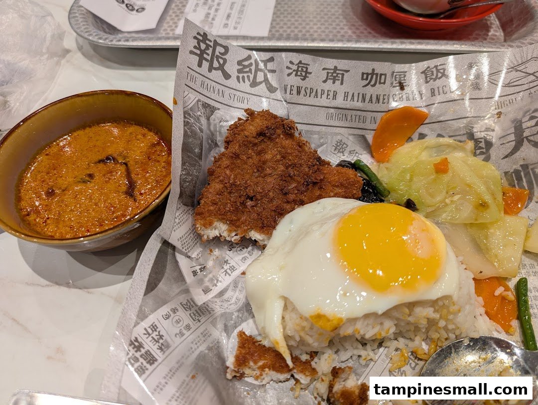 A close-up of Hainanese curry rice with crispy fried cutlet, a sunny-side-up egg, vegetables, and a side of rich curry.