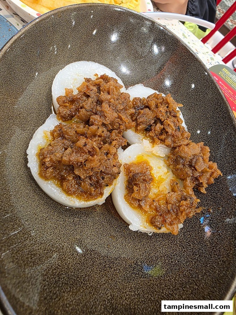 A close-up of traditional white steamed rice cakes topped with a savory, spicy dried radish relish.