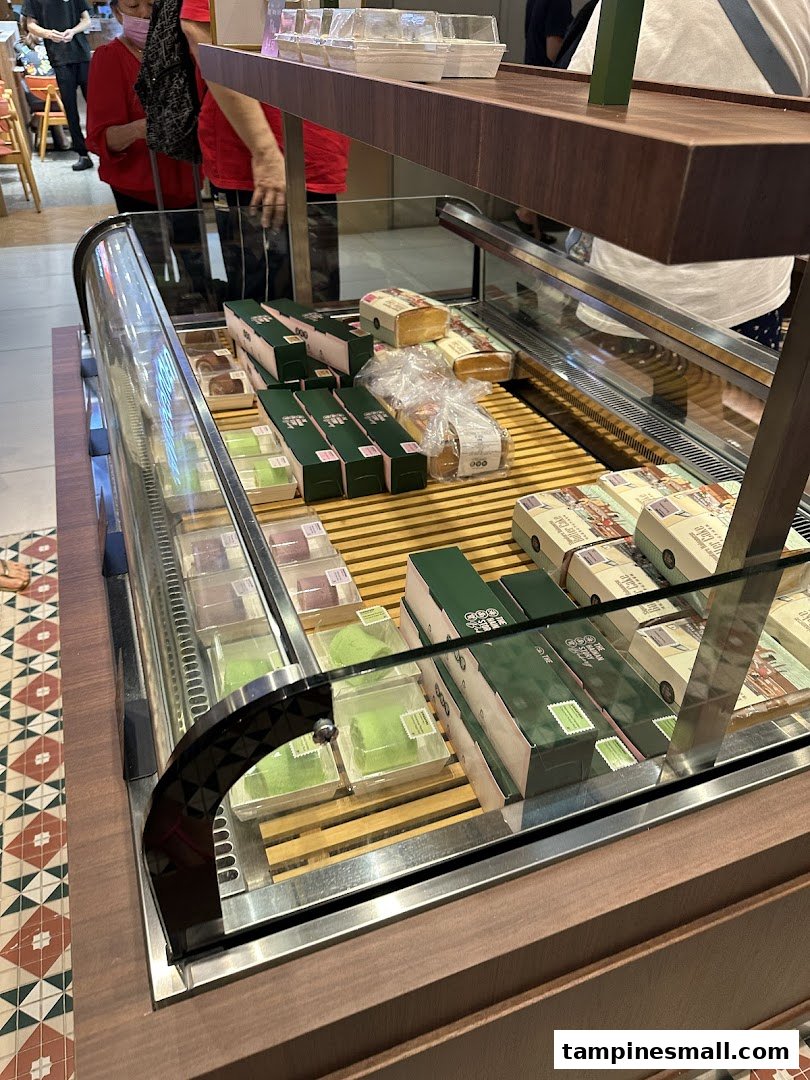 A glass display case showcasing a variety of packaged cakes and pastries, including green pandan rolls.