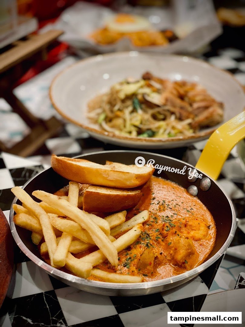 A close-up of a creamy seafood dish with fries and bread, alongside a noodle dish in the background.