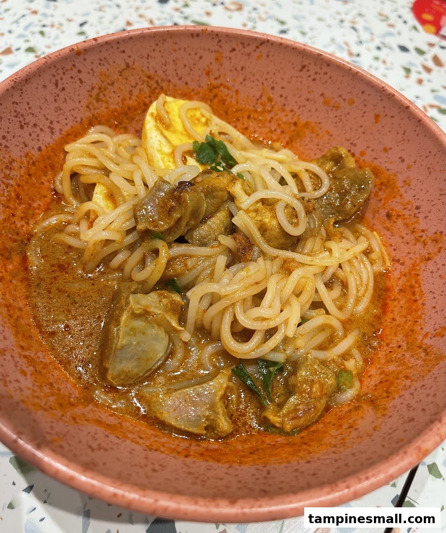 A close-up of a vibrant bowl of curry noodles with fishcake and egg, served in a pink bowl.
