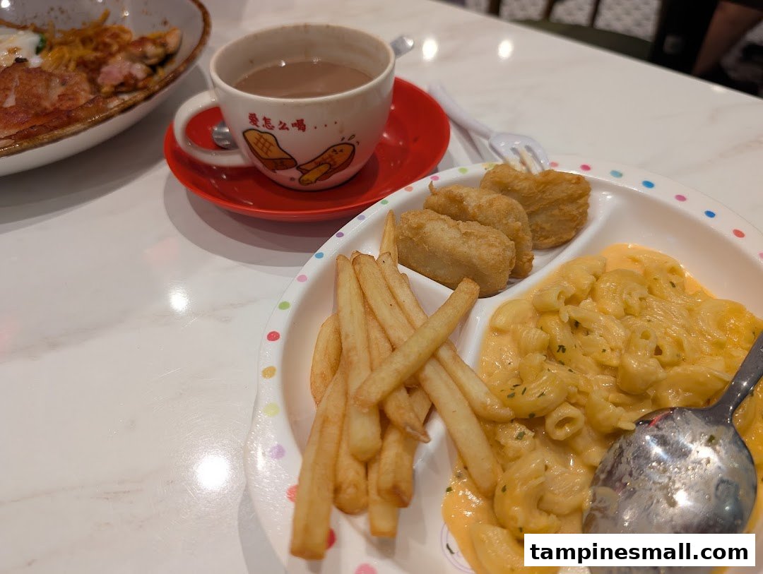 A delightful kids' meal featuring mac and cheese, fries, and nuggets, served with a warm beverage.