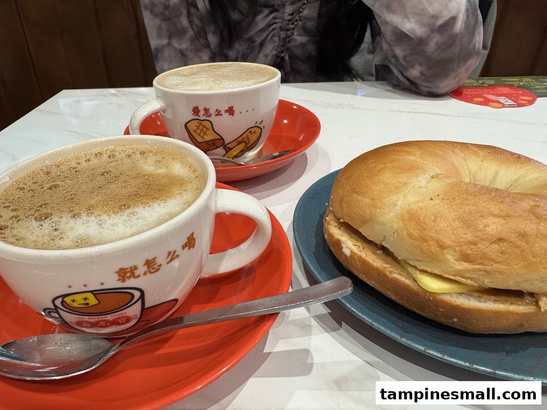 Two cups of coffee/tea with a bagel on a white table, showcasing a cozy cafe experience.