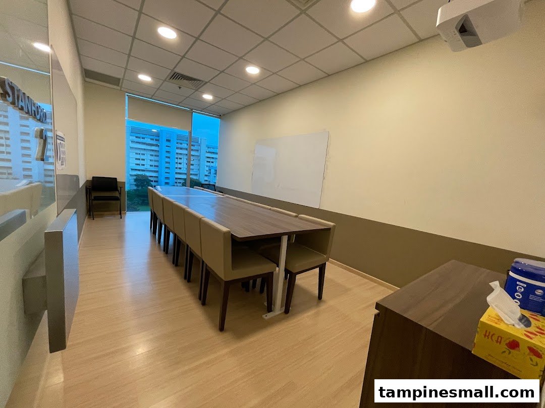 A spacious classroom or meeting room with a long table, chairs, whiteboard, and projector.