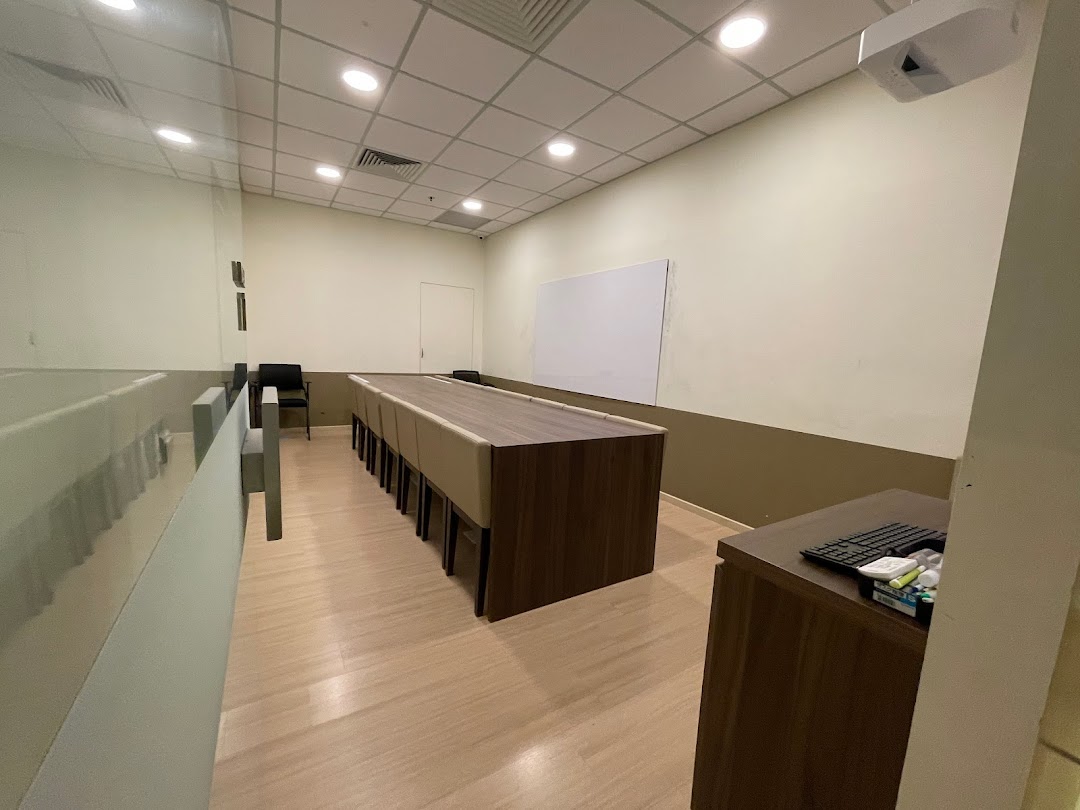 An interior view of a modern learning space with a long table, chairs, whiteboard, and projector.