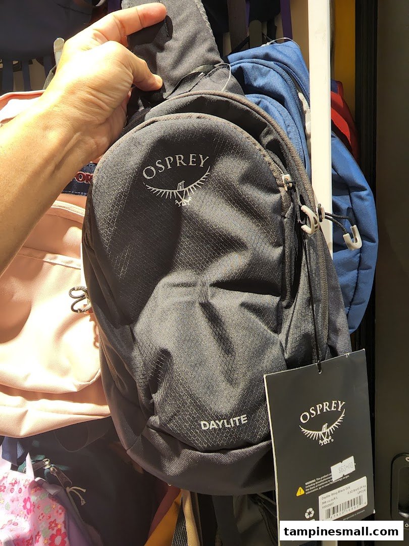 A hand holds a black Osprey Daylite sling bag with its price tag visible in a retail setting.