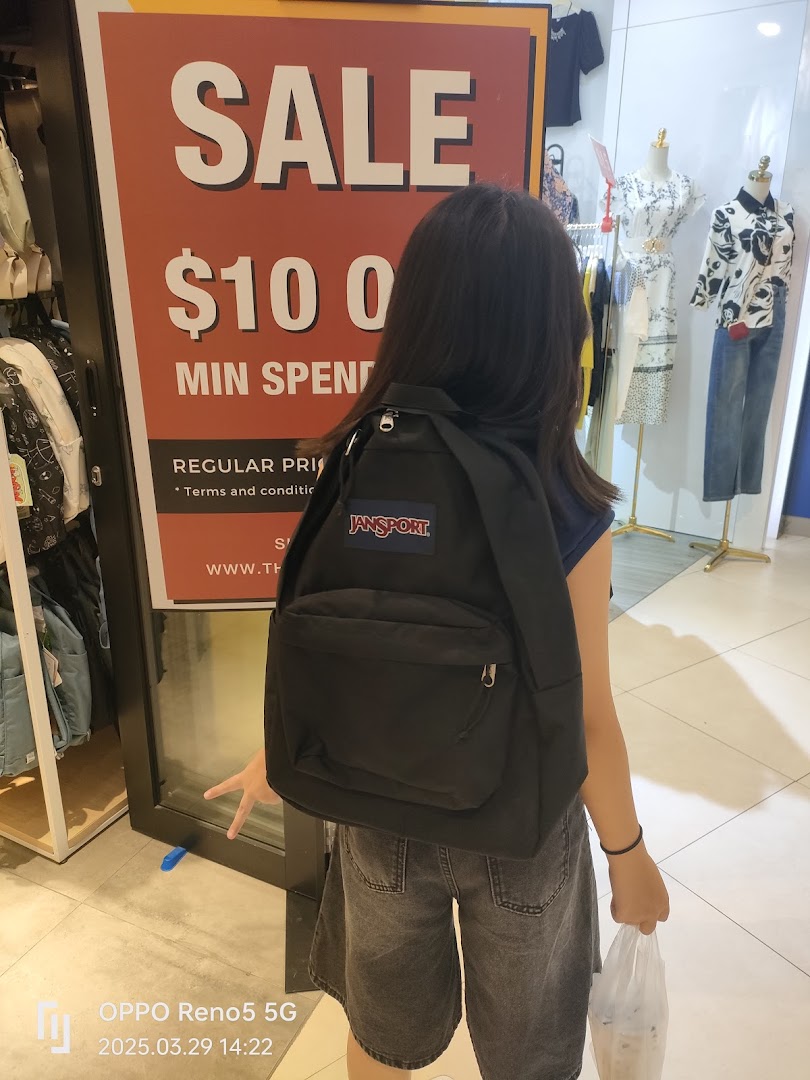A person stands inside a retail store next to a large sale sign, featuring clothing and accessories.