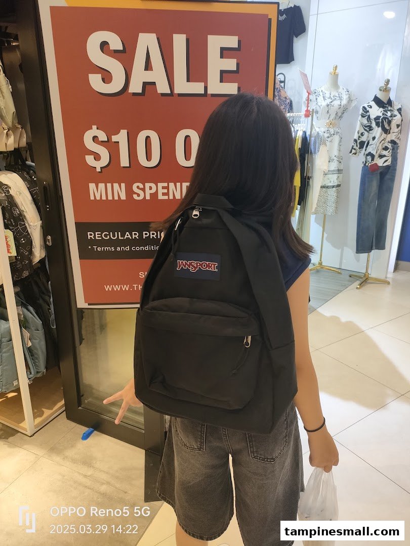 A person stands inside a retail store next to a large sale sign, featuring clothing and accessories.