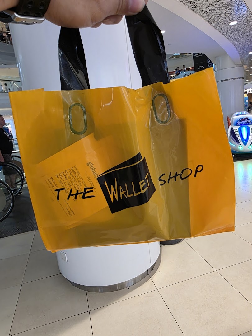 A person holds a yellow shopping bag from 'The Wallet Shop' inside a bustling mall.