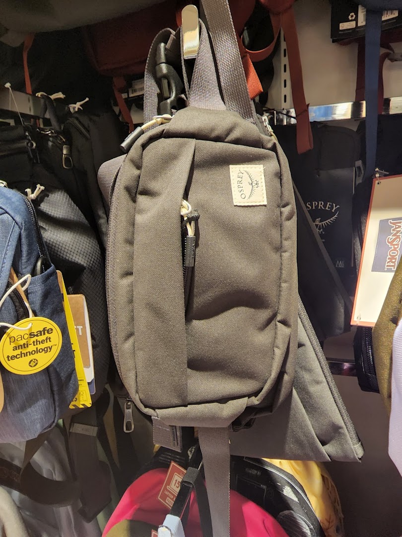 Various bags and travel accessories, including an Osprey sling bag, displayed in a retail store.