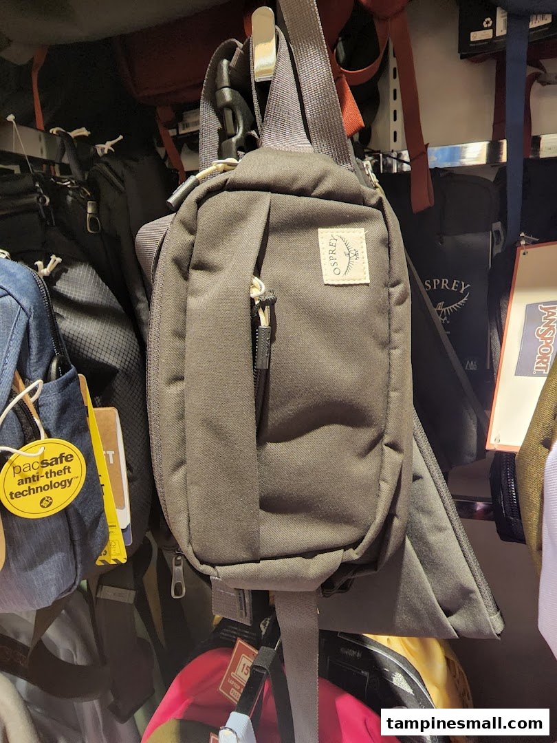 Various bags and travel accessories, including an Osprey sling bag, displayed in a retail store.