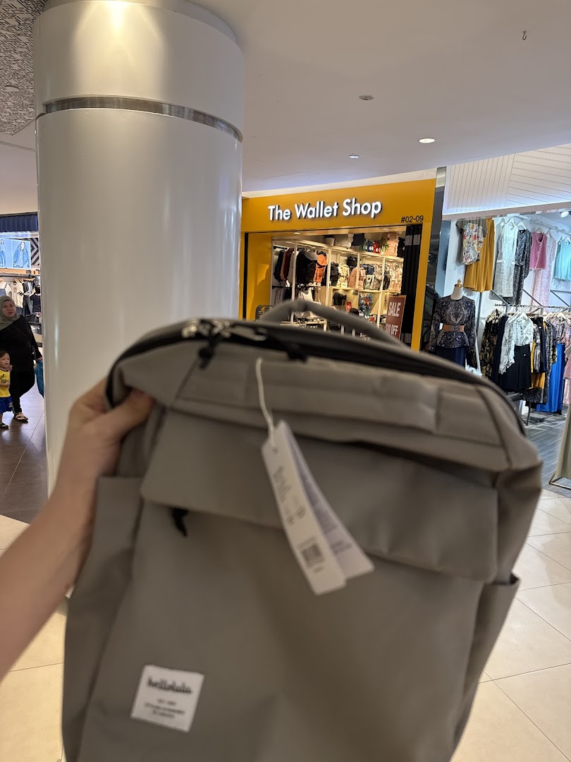 A person holds a grey bag in front of The Wallet Shop entrance, showcasing its bright yellow facade.