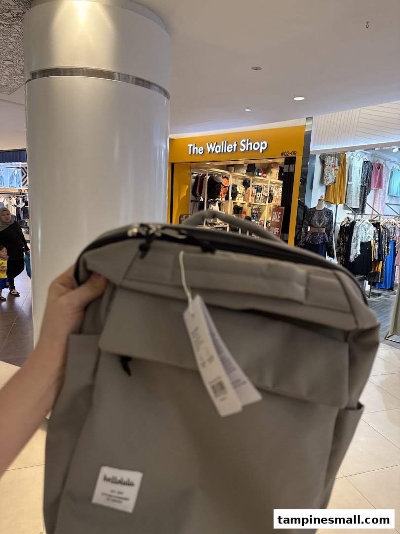 A person holds a grey bag in front of The Wallet Shop entrance, showcasing its bright yellow facade.