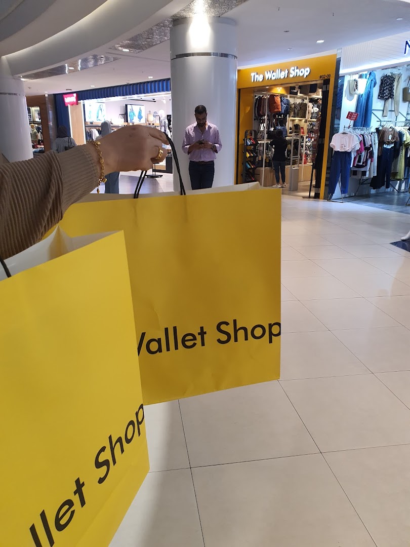 A shopper holds yellow bags from 'The Wallet Shop' with its entrance visible in a mall.