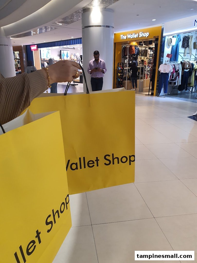 A shopper holds yellow bags from 'The Wallet Shop' with its entrance visible in a mall.