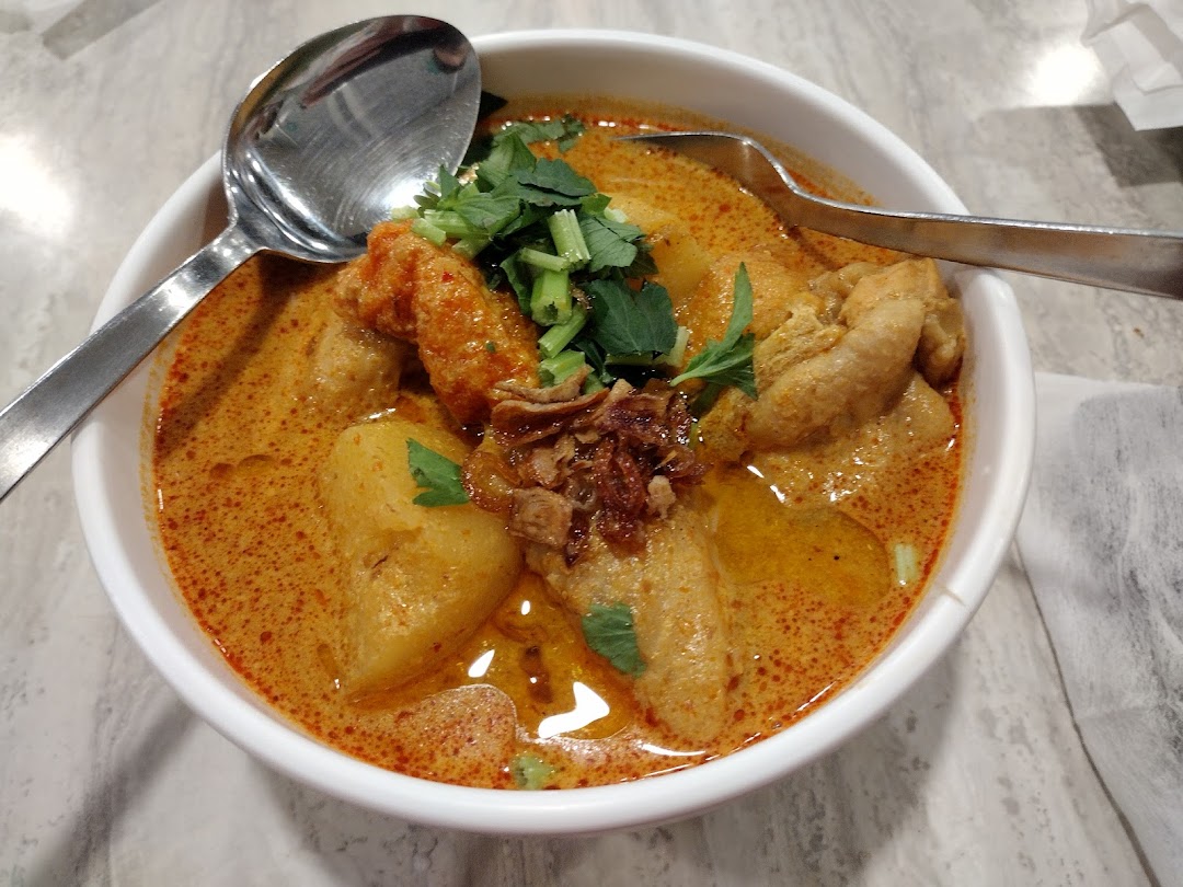 A close-up of a delicious bowl of curry noodles or laksa with various toppings and two spoons.