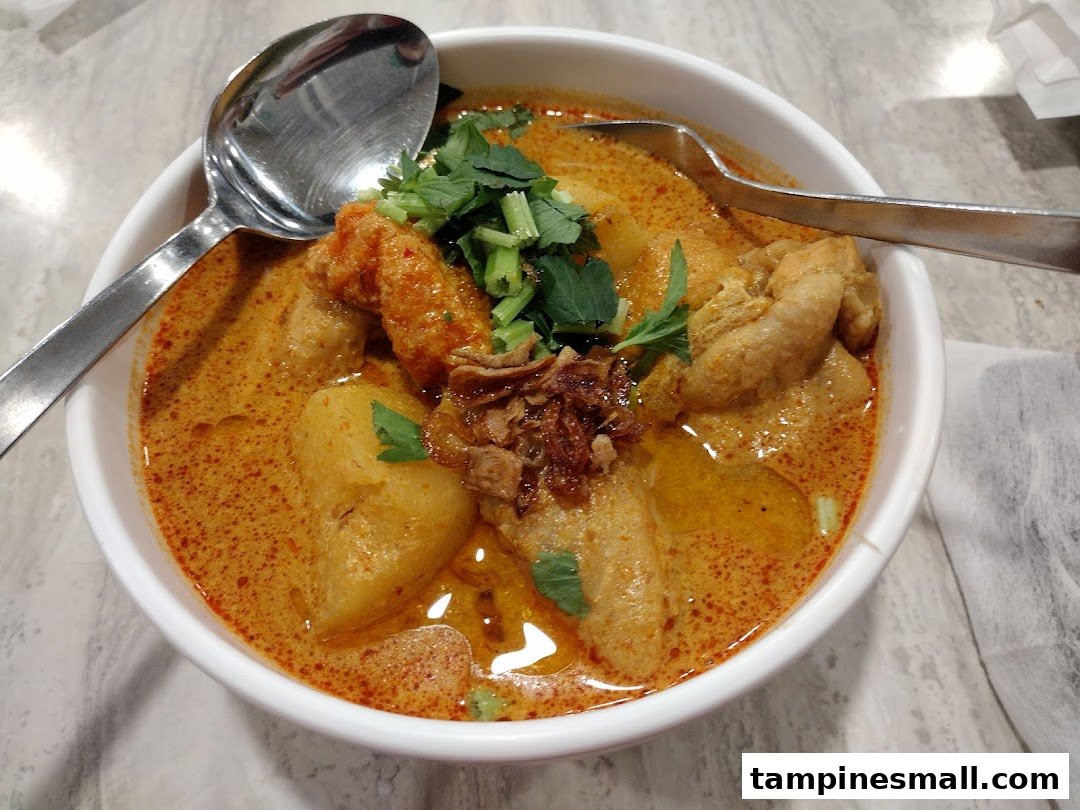 A close-up of a delicious bowl of curry noodles or laksa with various toppings and two spoons.