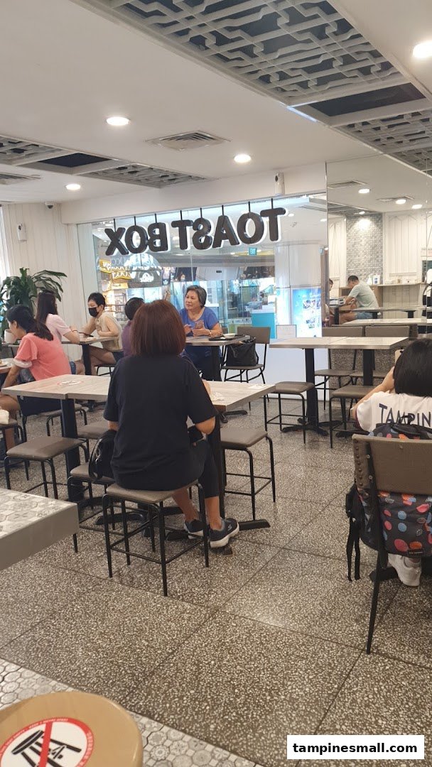 Customers enjoying a meal inside Toast Box, with the shop's name visible through the glass.