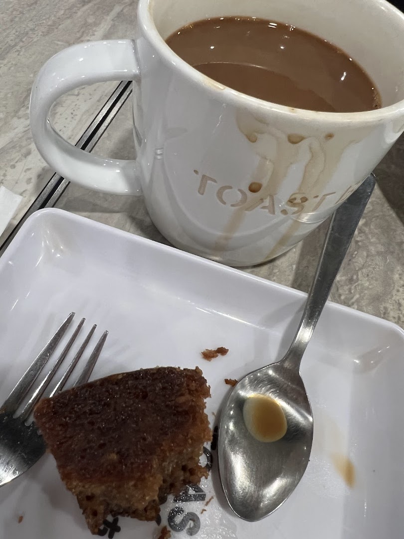 A close-up of a coffee mug with 'TOAST' and a partially eaten cake on a white plate.