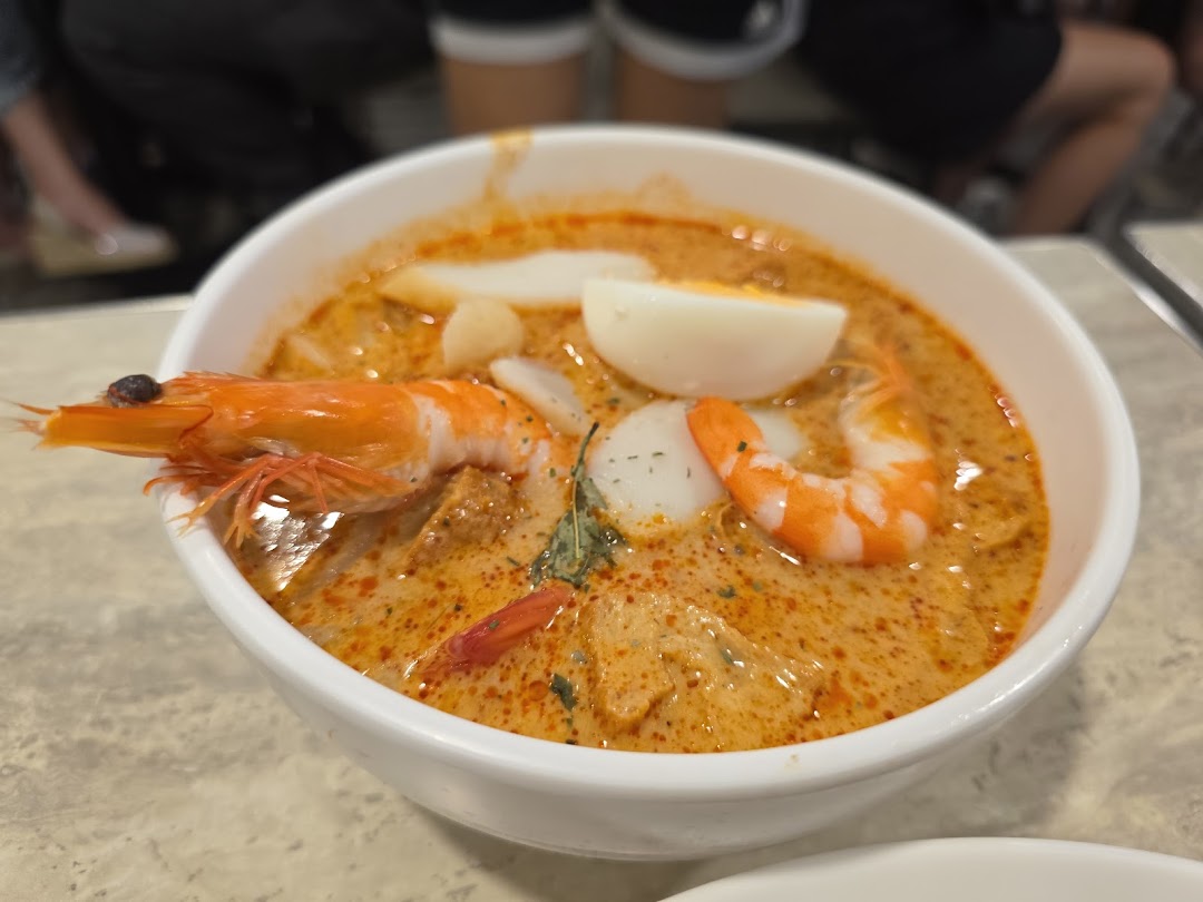A vibrant bowl of laksa with prawns, fish cake, and a hard-boiled egg.