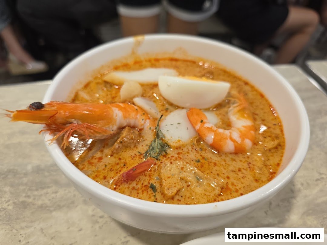 A vibrant bowl of laksa with prawns, fish cake, and a hard-boiled egg.