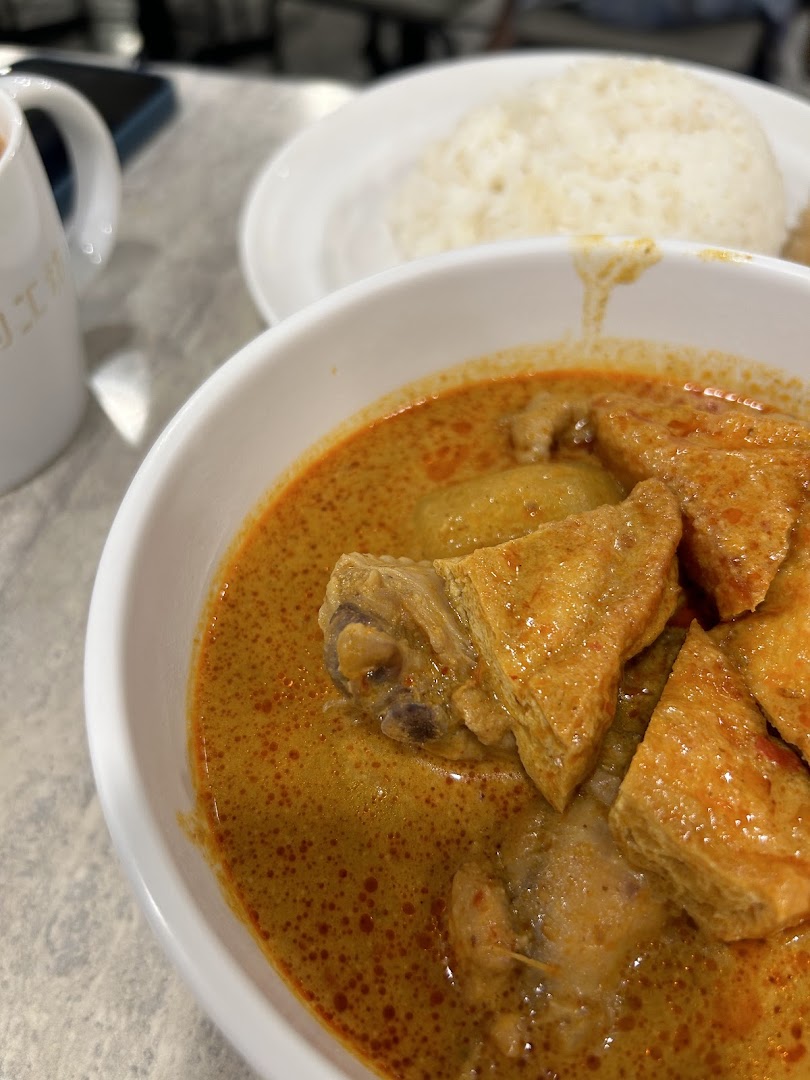 A close-up of a rich curry dish with chicken and tofu, served with rice and a beverage.