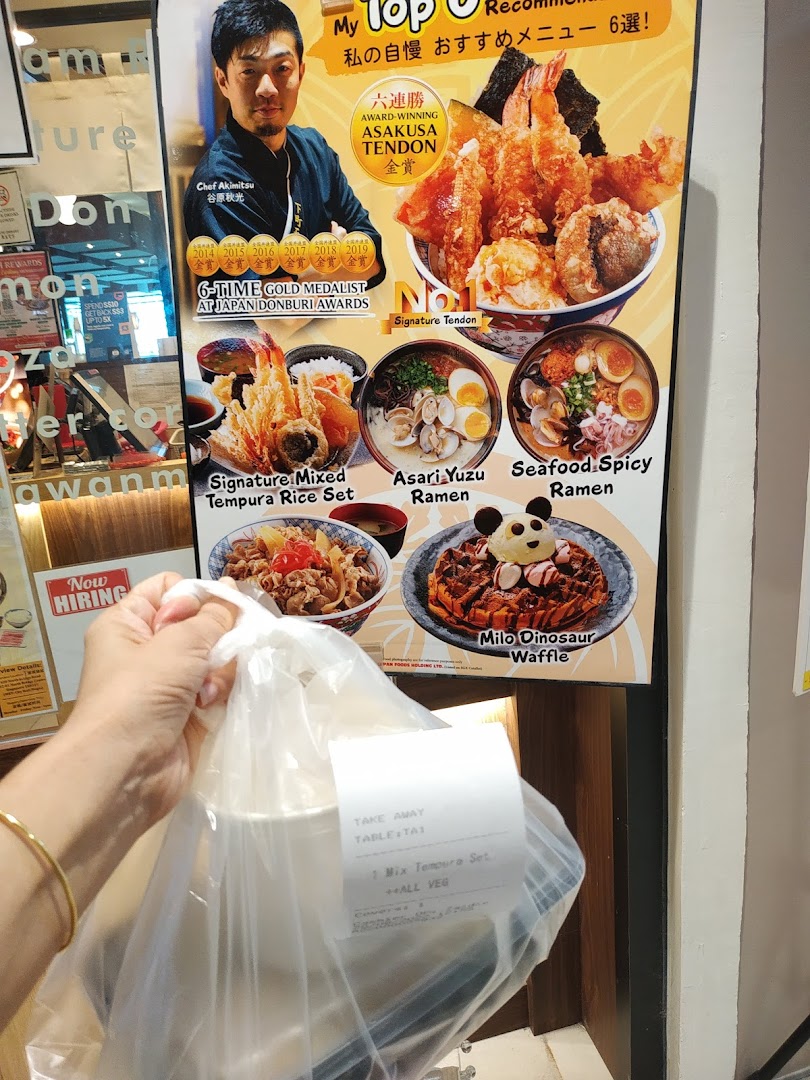 A customer holds a takeaway bag in front of Tokyo Shokudo's award-winning menu display.